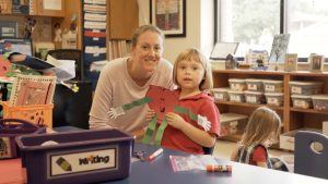 a teacher and young girl student posing for a picture in an elementary school classroom