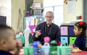 bishop Konderla sitting at a desk with catholic elementary school kids